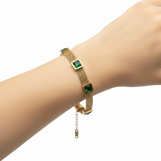 Gold bracelet with green square stones on a gray background
