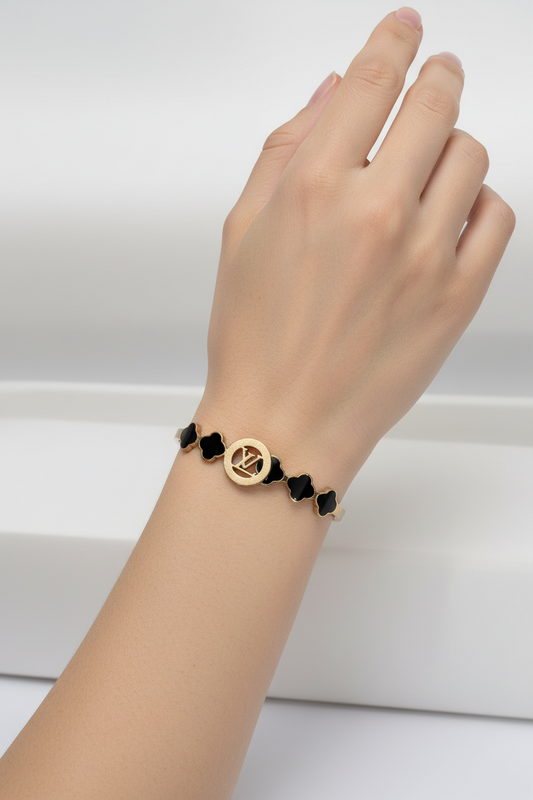 Gold bracelet with black clover-shaped links on a light gray background