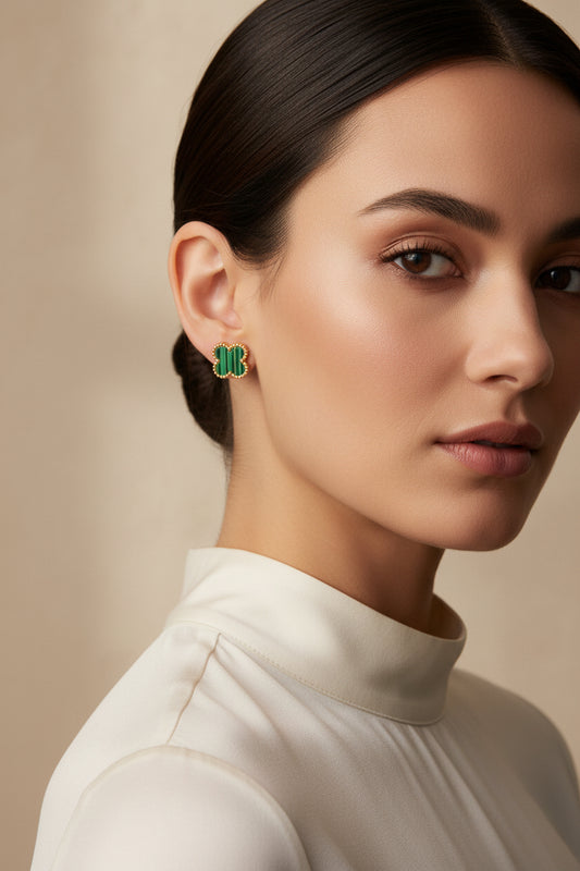 A pair of gold-tone four-leaf clover stud earrings with dark green malachite inlay, displayed on a light gray surface.