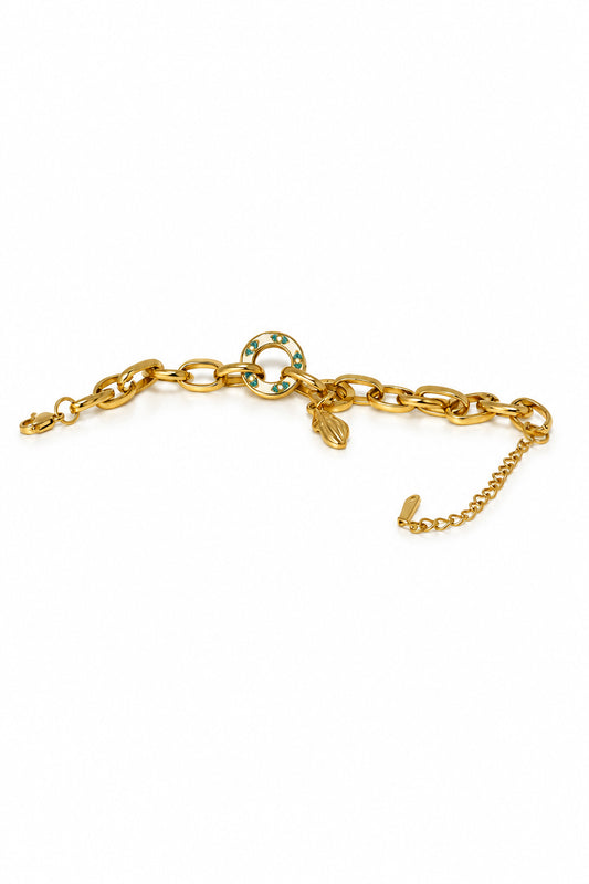 A gold chain bracelet with a circular interlocking link design and a small charm, displayed on a white curved tray against a textured light background.