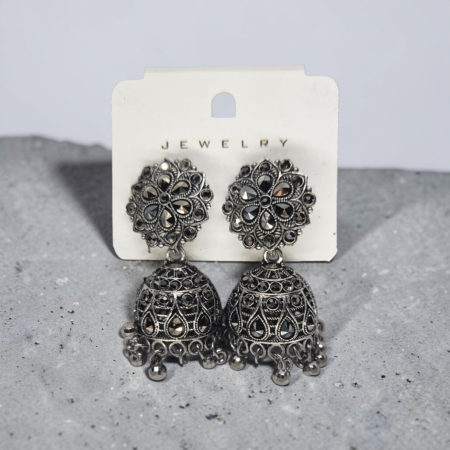 Pair of ornate silver earrings on a jewelry card against a gray background