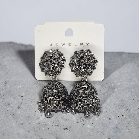 Pair of ornate silver earrings on a jewelry card against a gray background