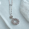 Silver necklace with a circular pendant on a light blue fabric background