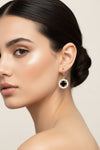 A pair of gold hoop earrings with oval dangles featuring a black clover motif surrounded by clear rhinestones, displayed on a white surface.
