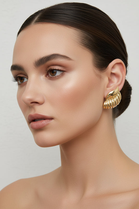 A pair of gold-toned textured stud earrings with a ribbed, segmented design and a smooth curved top accent, displayed on a light gray surface.