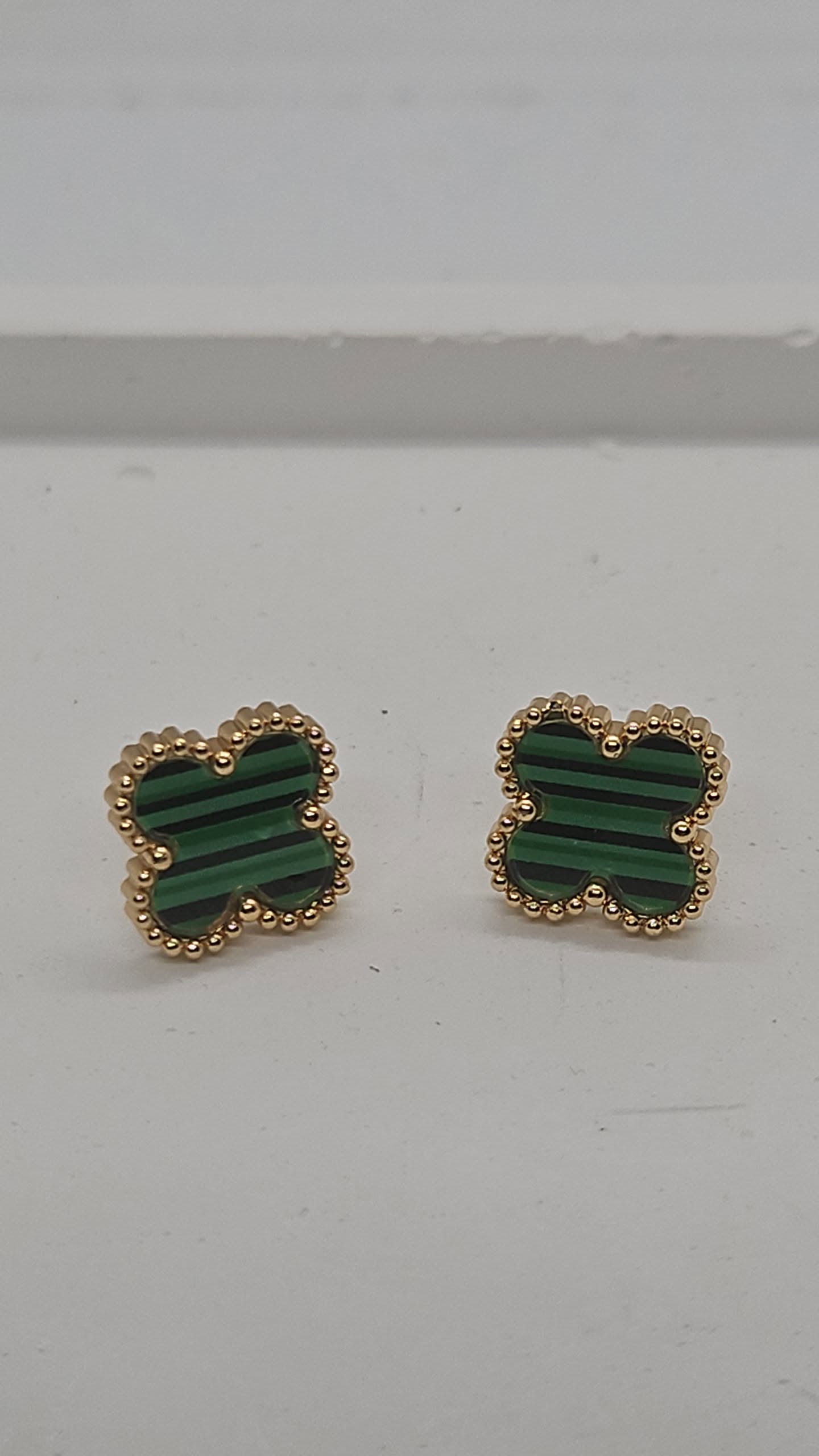 A pair of gold-tone stud earrings with green striped inlay, photographed on a plain light gray surface.
