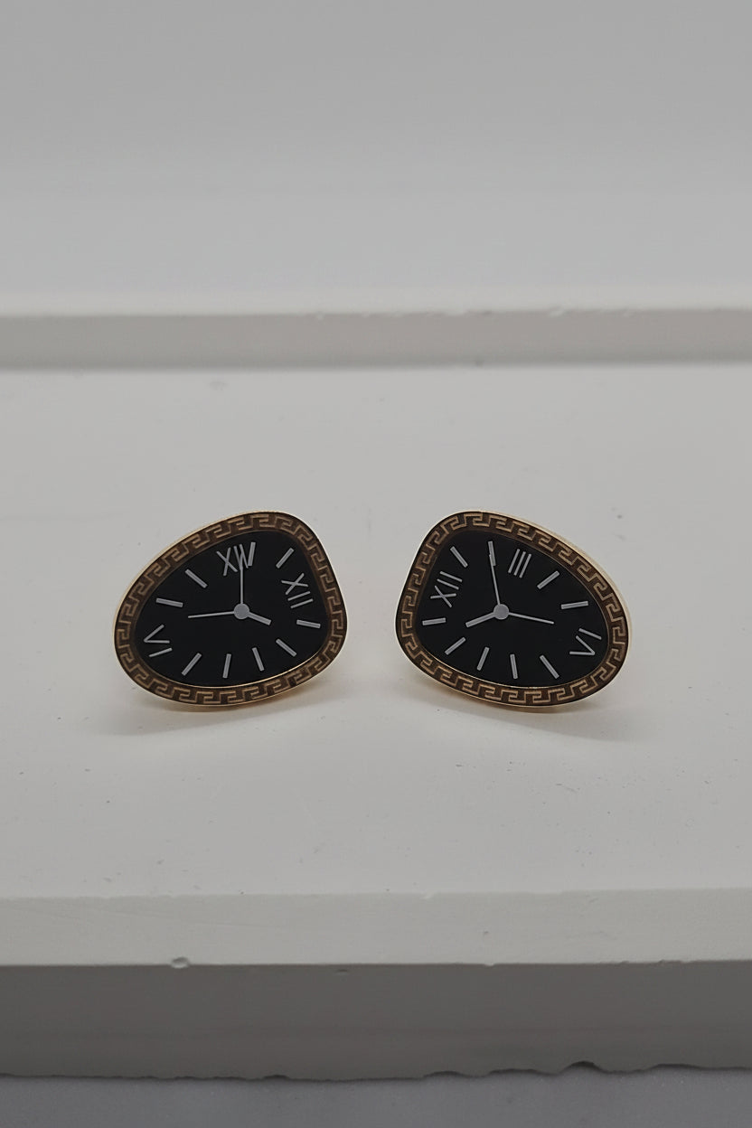 A pair of gold-tone triangular studs designed to look like clock faces with black centers and white hands.