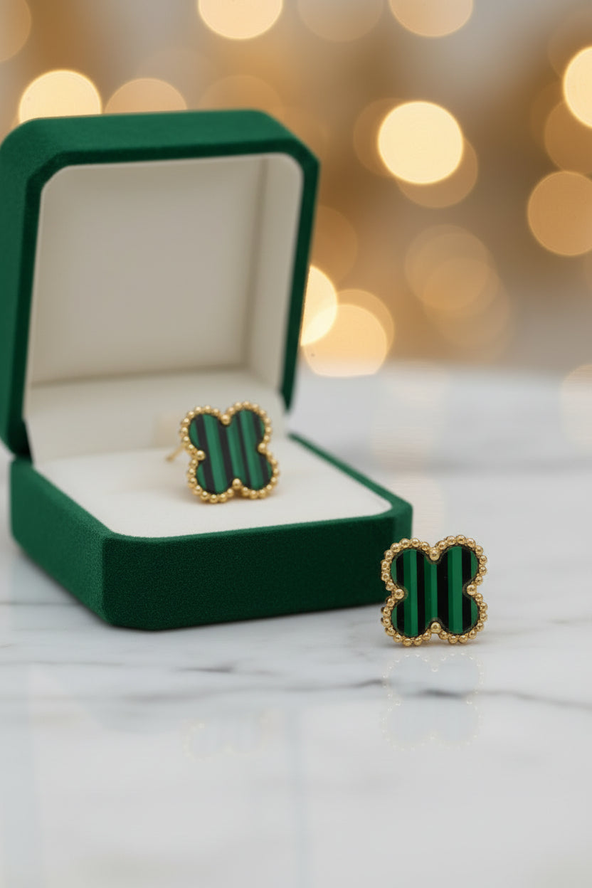 A pair of gold-tone stud earrings with green striped clover-shaped enamel inlays, displayed on a light gray surface against a white background.