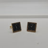A pair of square earrings designed to look like clock faces, featuring black centers with white numerals and hands, surrounded by gold-tone borders.