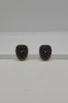 A pair of vintage-style clock face stud earrings with black enamel centers, gold-tone Roman numerals, and gold-tone bezels, displayed on a white surface against a light gray background.