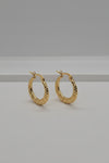 A pair of textured gold hoop earrings with fishhook backings, displayed on a light gray surface.
