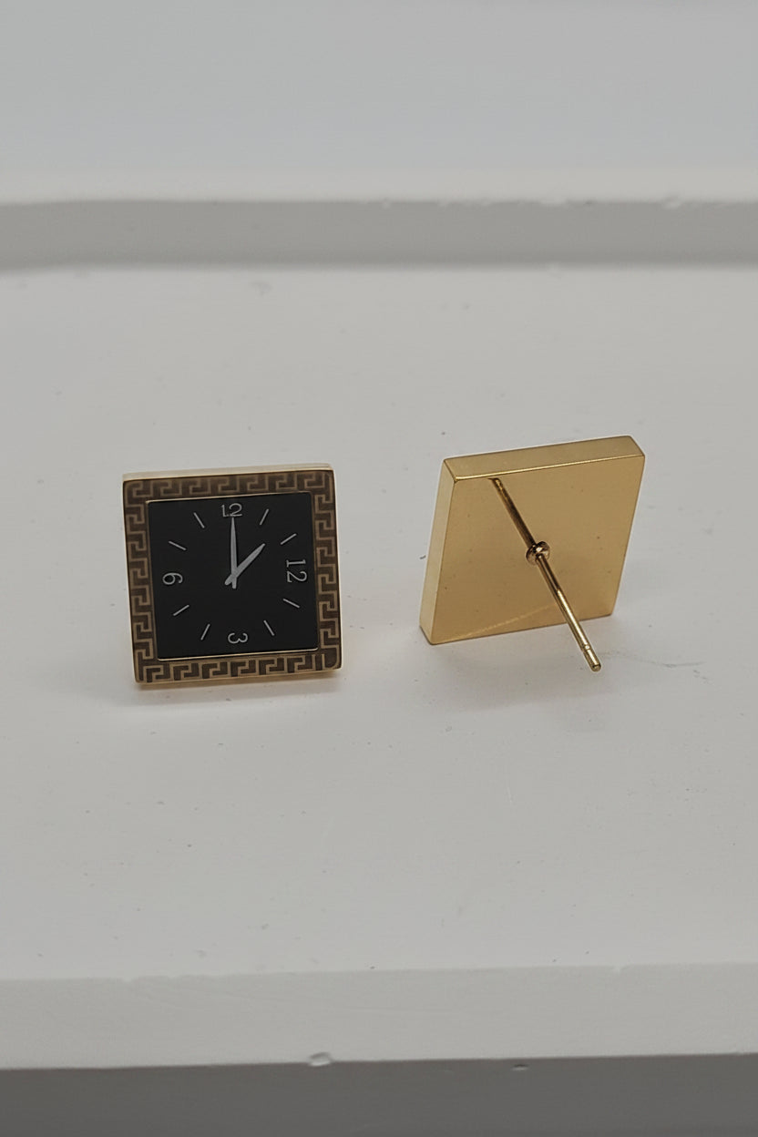 A gold square watch cushion and a matching square watch case with a black dial, displayed on a light gray surface.