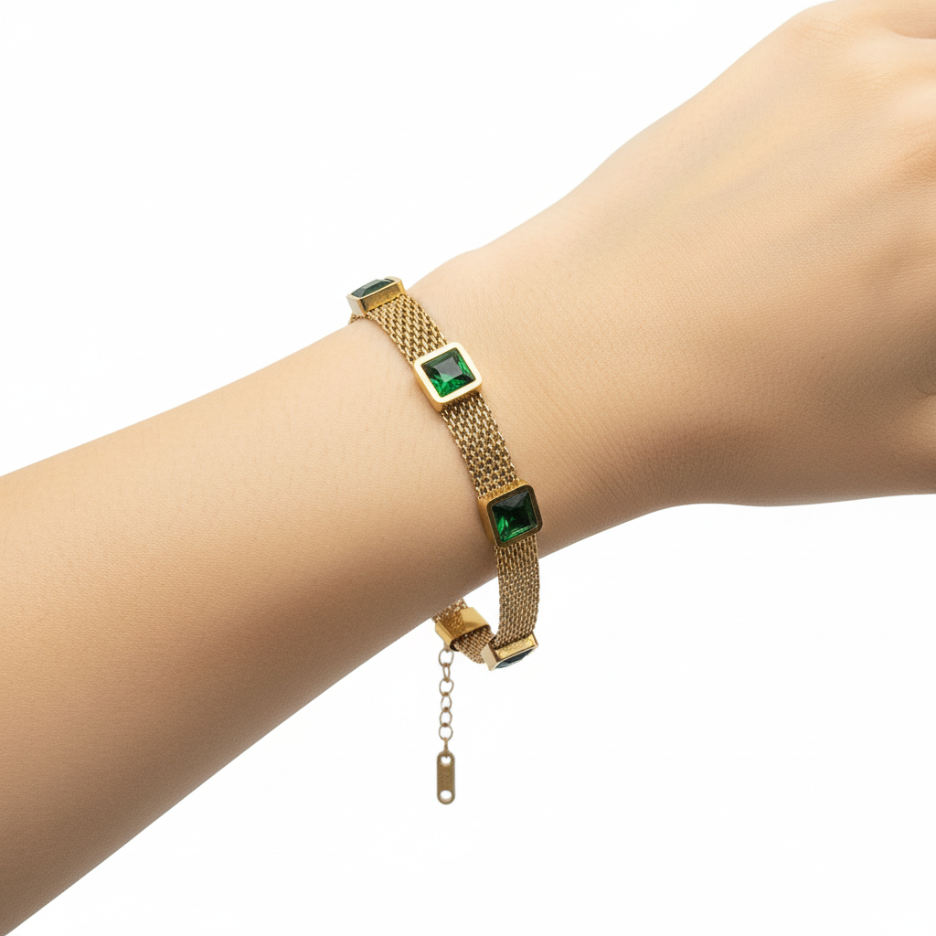 Gold bracelet with green square stones on a gray background