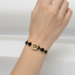 Gold bracelet with black clover-shaped links on a light gray background