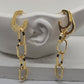 A pair of gold-toned hoop earrings with dangling chain-link drops, displayed on a white sculptural ear-shaped stand against a light gray background.
