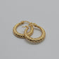 A pair of textured gold hoop earrings with a diamond-patterned beaded surface, displayed on a white textured stone surface.