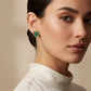 A pair of gold-tone four-leaf clover stud earrings with dark green malachite inlay, displayed on a light gray surface.