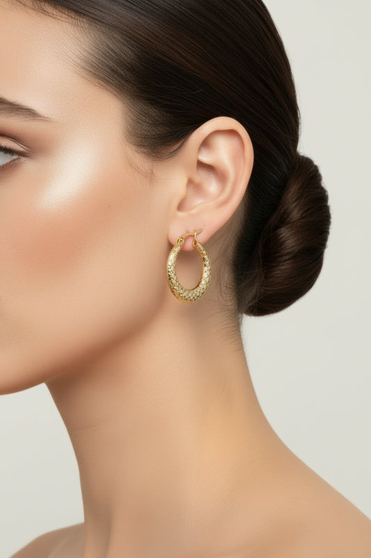 A pair of textured gold hoop earrings with fishhook backs, displayed on a light gray surface.
