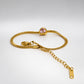 A gold-colored snake chain bracelet with a small pink heart-shaped crystal charm and an adjustable lobster clasp with a chain extender, displayed on a white surface.
