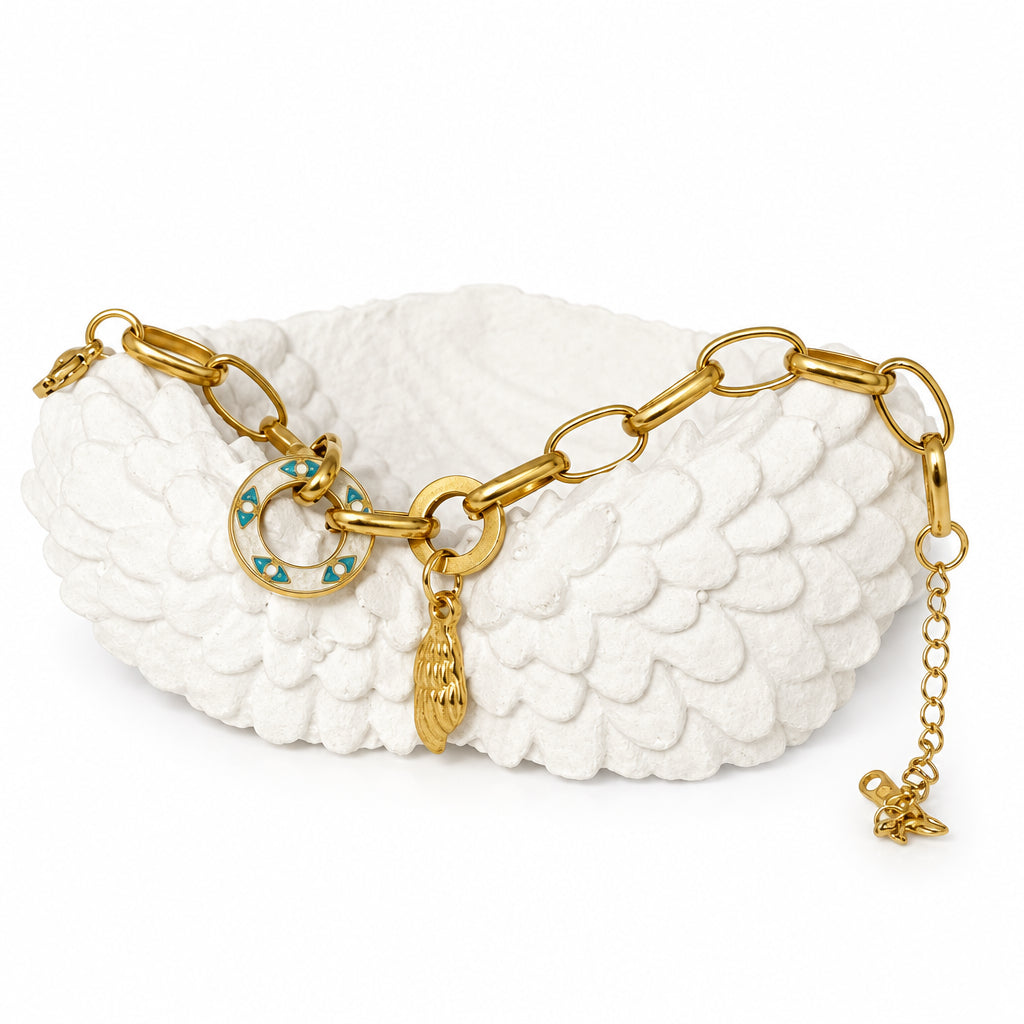 A gold-tone chain bracelet with a circular turquoise and gold charm, displayed on a white textured wing-shaped stand against a light beige background.