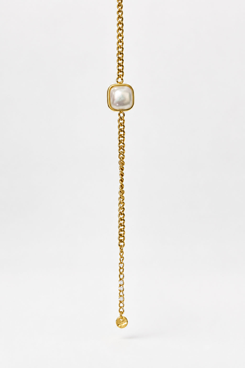 A gold chain bracelet featuring a central square bezel-set white pearl and a dangling chain with a small round gold bead at the end, displayed against a light beige background.