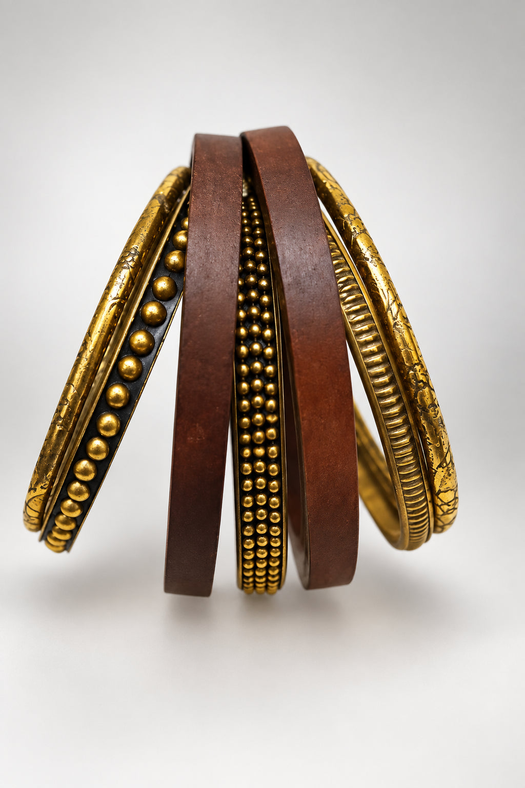A set of vintage bangles or wristlets hanging from a thin wire stand against a plain light background. The set includes three dark brown wooden pieces with rows of small metallic beads, two gold-toned metal pieces with beaded detailing, and two gold-toned pieces with a textured, ribbed outer surface.