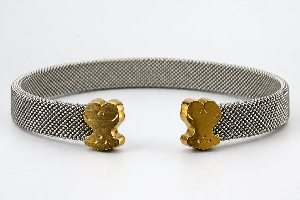 A silver-toned mesh cuff bracelet with two small gold-toned teddy bear charms, displayed on a white mannequin nose against a neutral light gray background.