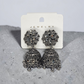 Pair of ornate silver earrings on a jewelry card against a gray background