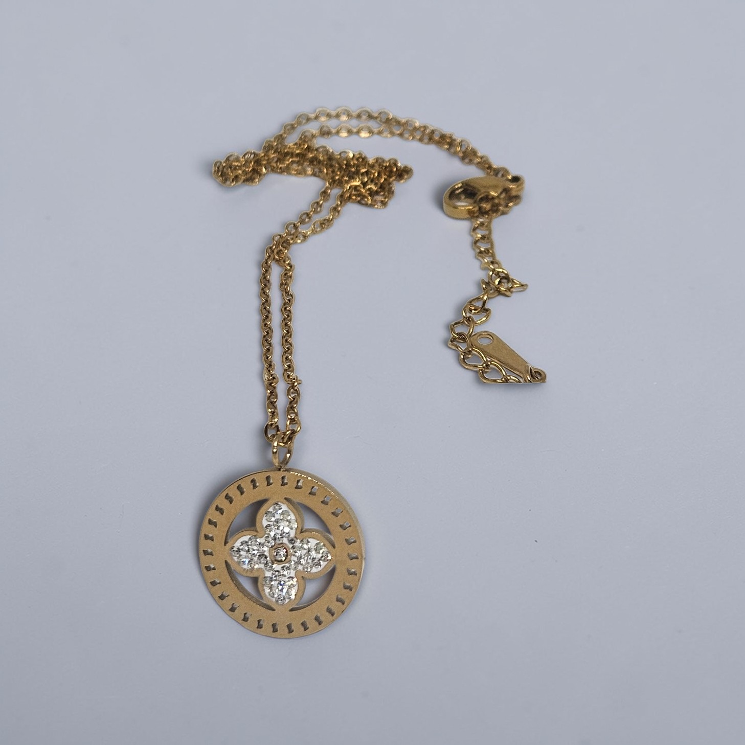 Gold necklace with a circular pendant featuring a diamond on a light gray background
