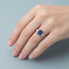 Silver ring with a blue gemstone and smaller diamonds on a textured light blue background