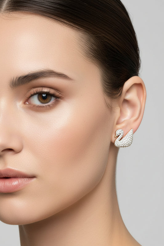 A pair of swan-shaped stud earrings covered in clear rhinestones on a silver-tone base, displayed on a light gray surface.