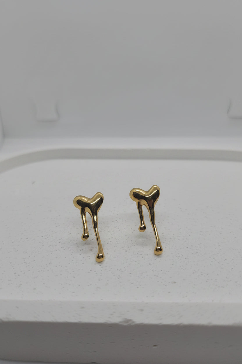 A pair of gold-toned, abstract-shaped stud earrings resting on a white display stand.