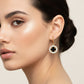 A pair of gold hoop earrings with oval dangles featuring a black clover motif surrounded by clear rhinestones, displayed on a white surface.
