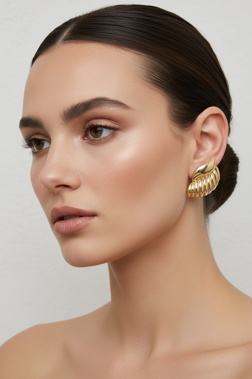 A pair of gold-toned textured stud earrings with a ribbed, segmented design and a smooth curved top accent, displayed on a light gray surface.