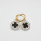 A pair of gold and silver hoop earrings with black clover motifs, displayed on a textured white surface.