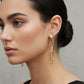 A pair of gold huggie hoop earrings with elongated link details, displayed on a white ceramic dish against a light gray background.
