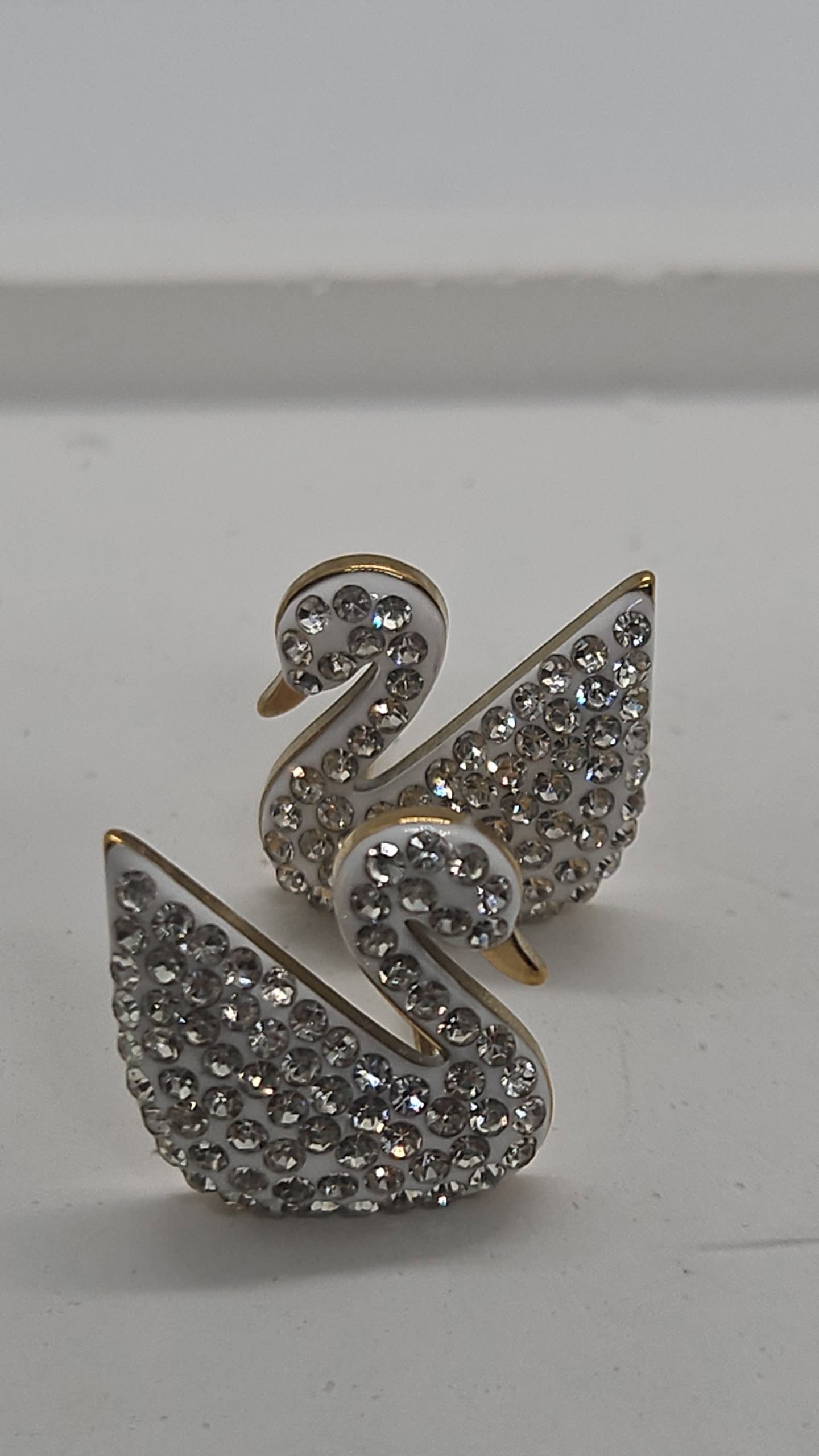 A pair of swan-shaped stud earrings covered in clear rhinestones with gold-tone outlines, displayed on a plain light gray surface.