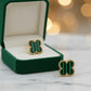 A pair of gold-tone stud earrings with green striped clover-shaped enamel inlays, displayed on a light gray surface against a white background.