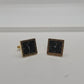 A pair of square earrings designed to look like clock faces, featuring black centers with white numerals and hands, surrounded by gold-tone borders.