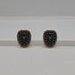 A pair of vintage-style clock face stud earrings with black enamel centers, gold-tone Roman numerals, and gold-tone bezels, displayed on a white surface against a light gray background.