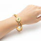 Gold bracelet with eye design and green gemstone on a white background