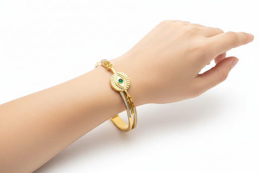 Gold bracelet with eye design and green gemstone on a white background