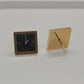 A gold square watch cushion and a matching square watch case with a black dial, displayed on a light gray surface.
